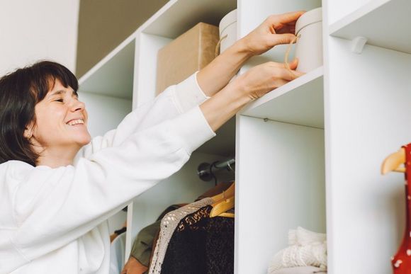 Person räumt eine weiße Box in einen weißen Kleiderschrank ein
